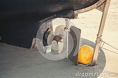 A view of the propeller of an old wooden boat with a yellow buoy on the beach Stock Photo