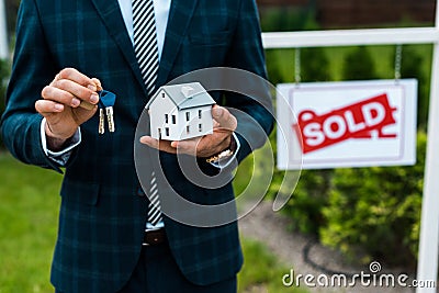 View of realtor holding carton house model and keys near board with sold letters Stock Photo