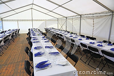 View of rented tent ready for guests. White table cloth, white plates with blue napkins and empty glass. Party celebration concept Stock Photo