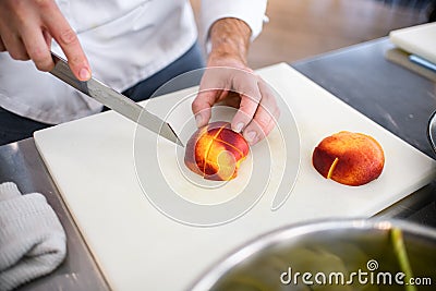 view of peach sliced on cutting board and male chef hand with knife nearby Stock Photo