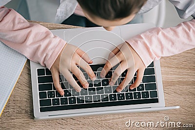 View of schoolkid using laptop while sitting at desk and doing homework Stock Photo
