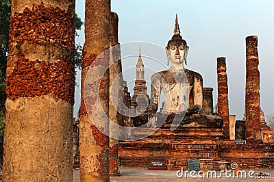 View of a seated Buddha statue among ruined columns in Wat Mahathat, an ancient Buddhist temple in Sukhothai Historical Park Stock Photo