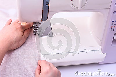 Female hands stitching light fabric on sewing machine at home. Stock Photo