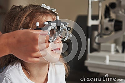 View from the side. Health care of the eyes. Doctor checking little girl sight and tuning the phoropter Stock Photo