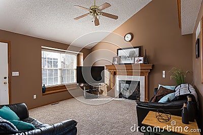 View of a simple living room with fireplace, television, sofa, couch, and a window in the brown wall Editorial Stock Photo