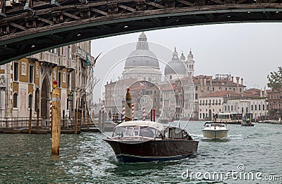 View of a small ferries on Canal Grande in a foggy day with historic Basilica di Santa Maria della Salute in the background in Ven Editorial Stock Photo