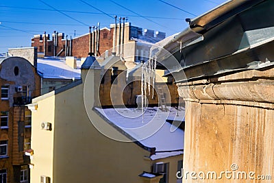 View of snow-covered roofs with spring icicles against blue sky Stock Photo