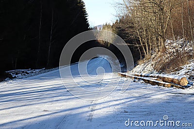 View of a snowy and icy road forest road. The trees illuminated by the sun and cast long shadows Stock Photo