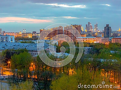 View of the spring evening city with blossoming trees, the setting sun and lights Stock Photo