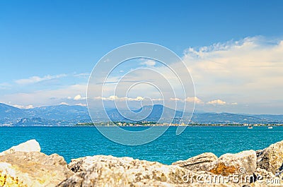 View from stone pier mole of Garda Lake azure water with Monte Baldo mountain range and Sirmione peninsula Stock Photo