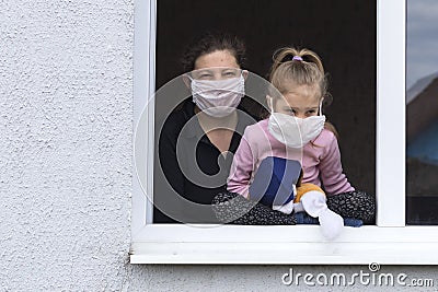 view from the street. In an open window, a woman holds a child, both masked. There is no way to take to the streets. Self- Stock Photo