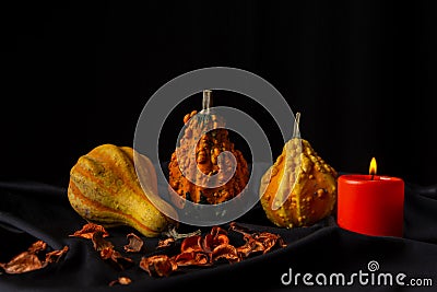 View of three pumpkins with orange candle on tablecloth and black background, horizontal Stock Photo