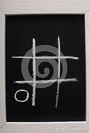 View of tic tac toe game on blackboard with chalk grid and naught on wooden surface Stock Photo