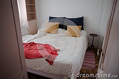 View to small cozy bedroom in old apartment through the open door. Bed covered with white blanket, blue and beige pillows Stock Photo