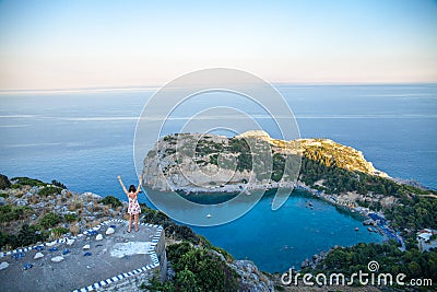 View from top on Anthony Quinn Bay and beach, Rhodes in Faliraki, Greece. Happy girl Raising One Hand. Beautiful beach and bay on Editorial Stock Photo