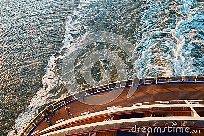 View from the top at the back deck of the cruise ship, leaving foamy trace on the water and waves in the ocean during sunset. Stock Photo