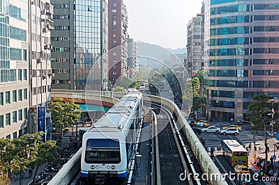 View of a train traveling on elevated tracks of Taipei Metro System between office towers under blue clear sky Stock Photo