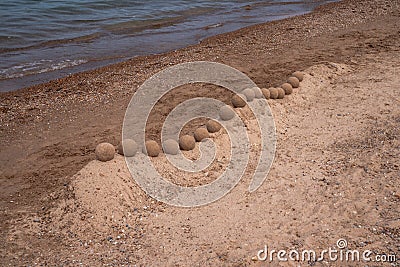 View of an undulating sand castle hill or wall with perfectly smooth round balls or spheres of wet sand placed on the ridge that Stock Photo