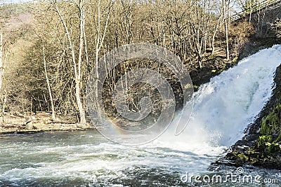 View of a waterfall with a rainbow reflected in the water with an arid vegetation in the background in the small city of Spa Belgi Stock Photo