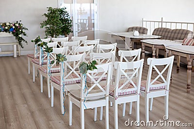 View of a wedding ceremony scene in a room with several rows of white chairs and compositions from different flowers Stock Photo