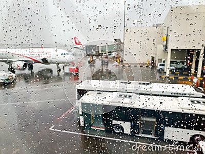 View through wet window and water droplets on airpalne and airport terminal during rain Stock Photo