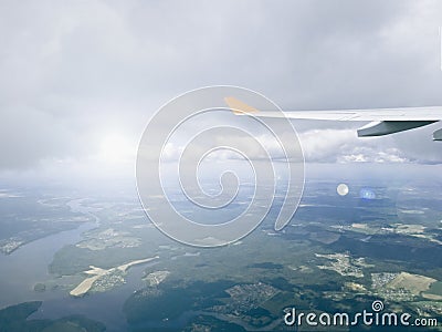 View from the window of the aircraft on the endless fields and forests, clouds and the wing of the aircraft with a glint of light Stock Photo