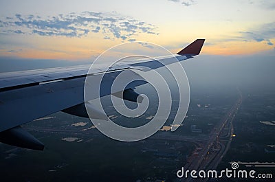 View of the wing of the plane and the city and the road in the morning at dawn. Stock Photo