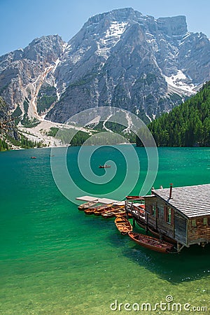 view of wooden house on water with pier and boats lake in dolomites mountains Stock Photo