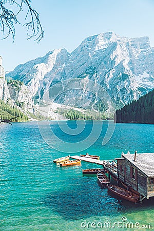 view of wooden house on water with pier and boats lake in dolomites mountains Stock Photo
