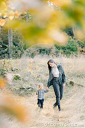 View through the yellow leaves on the mother with a little girl walking on a green meadow Stock Photo