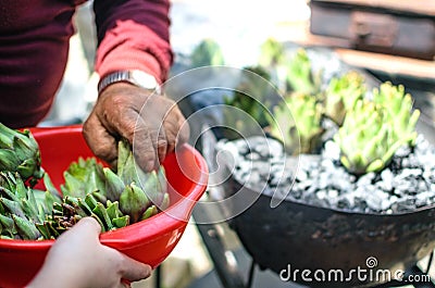 View of young hand giving artichokes to elder hands in a red bowl Stock Photo