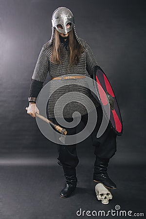 Viking stands with an ax on a gray background. A man in chain mail and a helmet stepped on the enemy`s skull. Medieval warrior in Stock Photo