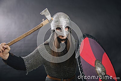 Viking stands with an ax on a gray background. A man in chain mail and a helmet waves his weapon. A medieval warrior in armor goes Stock Photo