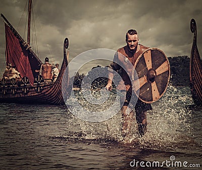 Viking warrior in the attack, running along the shore with Drakkar on the background. Stock Photo