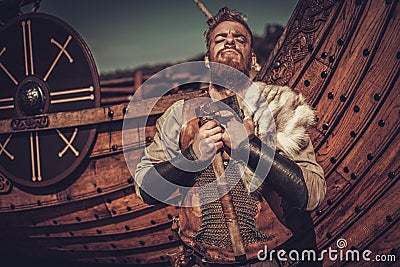 Viking warrior with axes standing near Drakkar on the seashore. Stock Photo