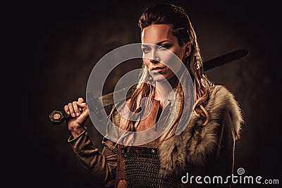 Viking woman with sword in a traditional warrior clothes, posing on a dark background. Stock Photo