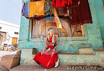 Village house and young woman sitting at front of colorful building in small indian town. Editorial Stock Photo