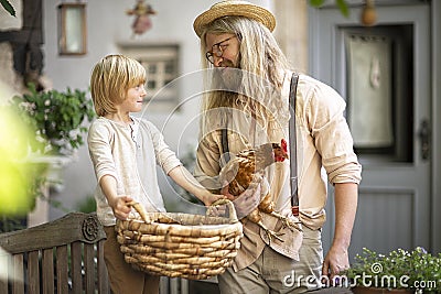 Village life. Country boy with Daddy brown chicken and a big basket in the yard near the front door.Summer day Stock Photo