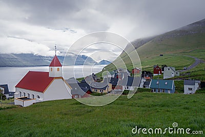 Village of Mikladalur in Kalsoy, Faroe Island. White wooden church with fjord and village in the background Stock Photo