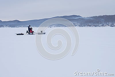 The snowmobile with fishermen is riding along the winter lake. Editorial Stock Photo