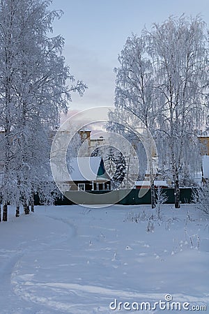 A village private house behind a fence, snow-covered trees. The path through the snowdrift in a winter park. Stock Photo