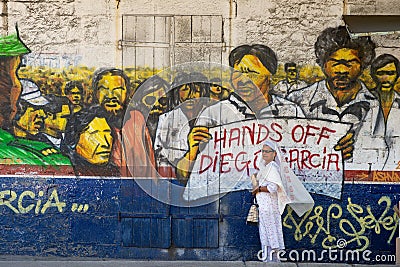 Woman stands at the street with political poster `Hands off Diego Garcia` painted at the wall in Ville Noire, Mauritius island. Editorial Stock Photo