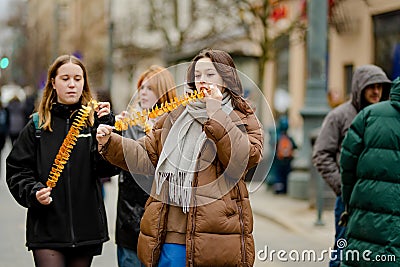 VILNIUS, LITHUANIA - MARCH 4, 2022: Cheerful young women eating fried potato on a stick on cold winter day outdoors Editorial Stock Photo