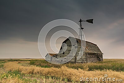 Vintage barn, bins and windmill under ominous dark skies in Saskatchewan, Canada Stock Photo