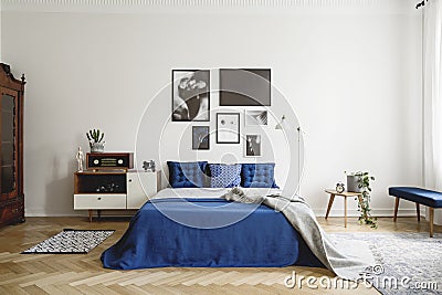 Vintage bedroom interior with bedside table, king size bed with blue bedding and pillows. Mockup gallery on the white wall Stock Photo