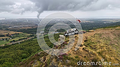 Vintage burnt-out vehicle sits atop a hill with a nearby flag waving in the breeze Stock Photo