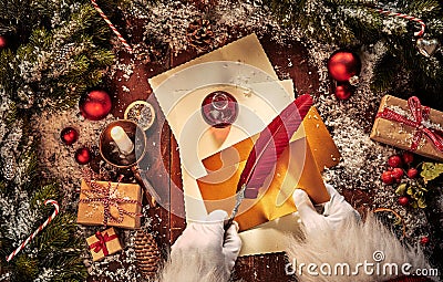 Vintage Christmas scene with Santa Claus writing a letter with a feather quill pen and decorations on a rustic table with Stock Photo