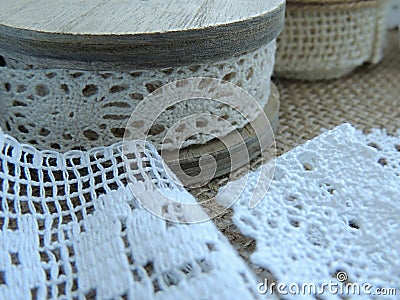 Vintage cream lace on wooden bobbin, white lace on burlap background. Stock Photo