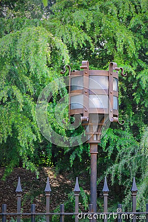 Vintage decorative electric street lamp behind iron fence in nat Stock Photo