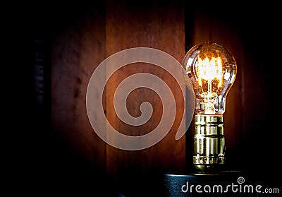 Vintage Edison light bulb illuminates on wood background. Stock Photo